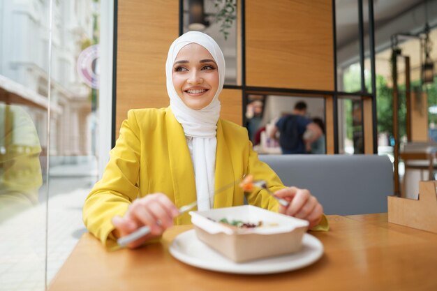 Joven musulmana en hijab almorzando en el café