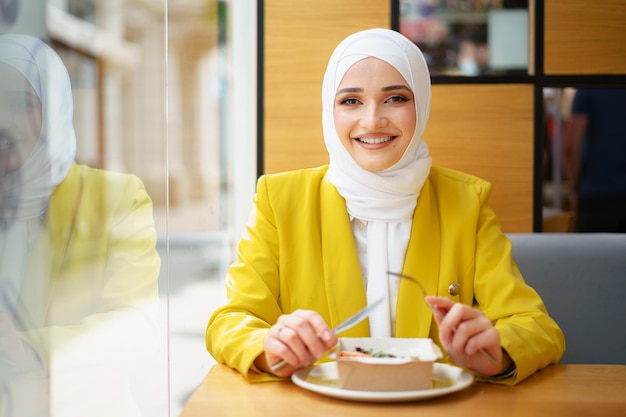 Joven musulmana en hijab almorzando en el café