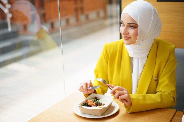 Joven musulmana en hijab almorzando en el café