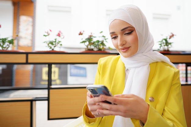 Joven musulmana en hijab con su teléfono inteligente en el café