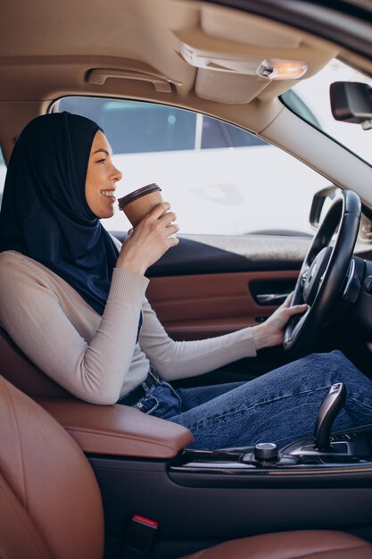 Joven musulmana moderna tomando café en el coche