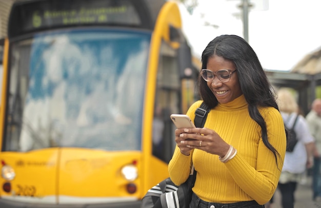 Foto gratuita joven negra en la estación de tranvía aun usa un teléfono inteligente