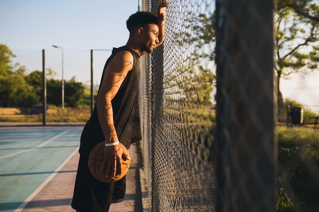 Joven negro haciendo deporte, jugando baloncesto al amanecer, estilo de vida activo, mañana de verano