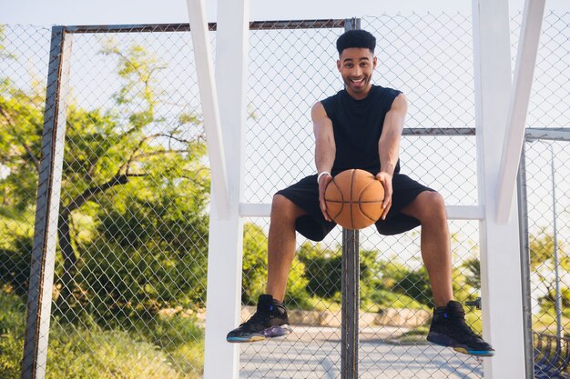 Joven negro haciendo deporte, jugando baloncesto, estilo de vida activo, mañana de verano, sonriendo feliz divirtiéndose