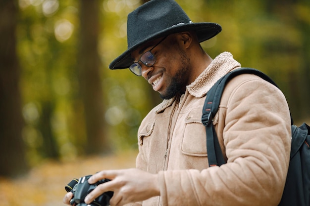 Joven negro de pie en la carretera en el bosque con una cámara. Fotógrafo masculino caminando en un bosque