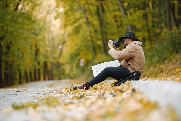 Joven negro sentado en la carretera en el bosque con una cámara. Fotógrafo masculino en un bosque