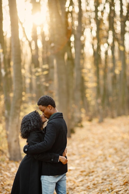 Joven negro y su novia abrazándose. Pareja romántica caminando en el parque de otoño. Hombre y mujer con abrigos negros.