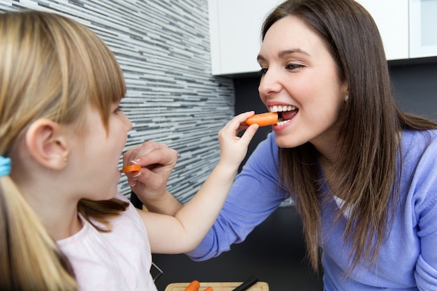 Joven y niña comiendo zanahorias en la cocina