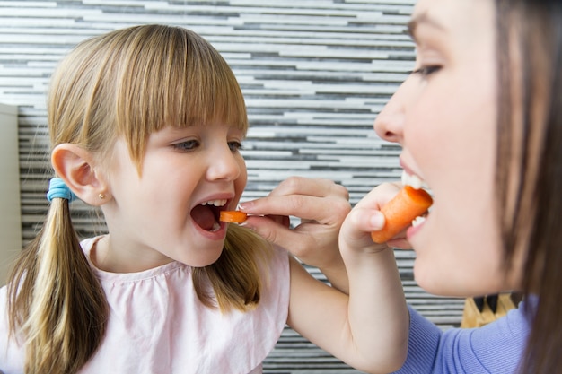 Joven y niña comiendo zanahorias en la cocina