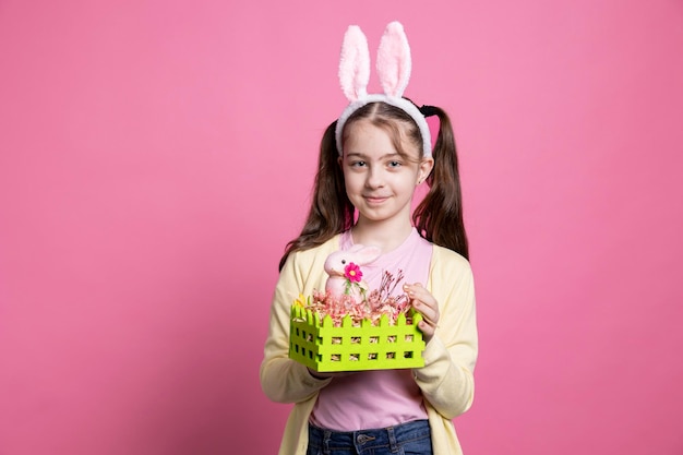 Foto gratuita joven niña optimista mostrando una canasta hecha a mano decorada con huevos y un conejo