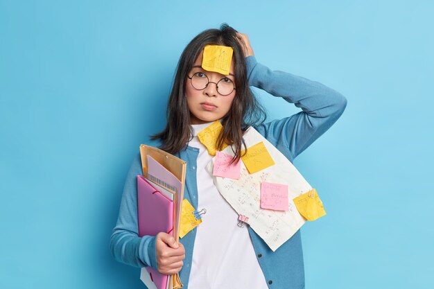 Joven olvidadiza decepcionada cansada de abarrotar para el examen mantiene la mano en la cabeza y parece estresada.