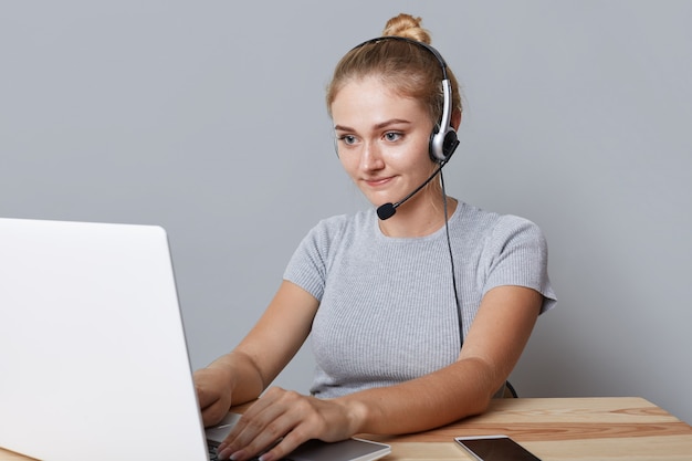 Foto gratuita la joven operadora o consuladora tiene auriculares, mira la computadora portátil, hace videollamadas, usa conexión a internet de alta velocidad