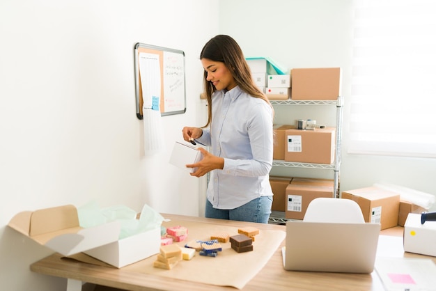 Joven orgullosa preparando muchos paquetes en la tienda de su oficina. Emprendedor exitoso listo para enviar productos de belleza orgánicos