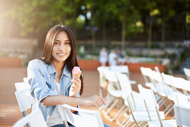 Joven oriental comiendo helado al aire libre en un parque de la ciudad o en un concierto esperando para comenzar el concepto de estilo de vida