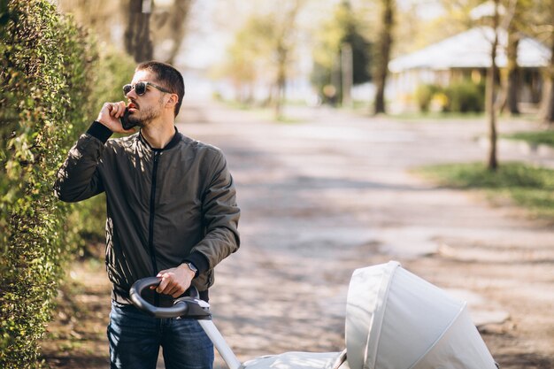 Joven padre caminando con carro de bebé en el parque