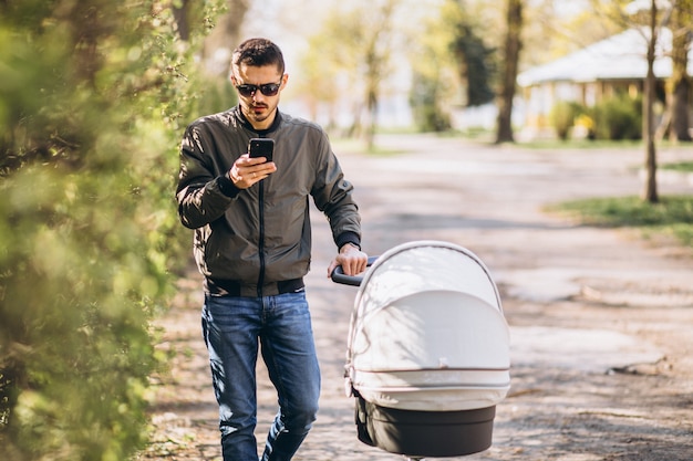 Joven padre caminando con carro de bebé en el parque