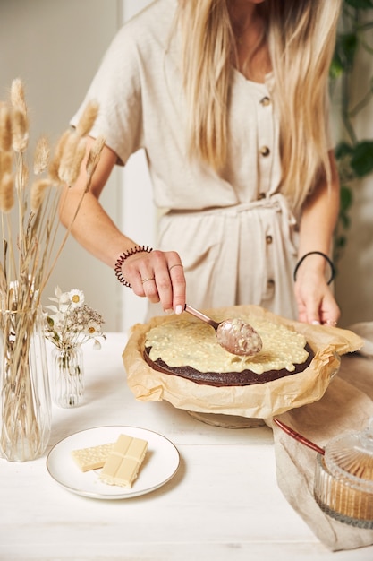 Joven panadero haciendo un delicioso pastel de chocolate con crema sobre una mesa blanca