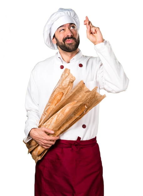 Joven panadero sosteniendo un poco de pan y con sus dedos cruzando