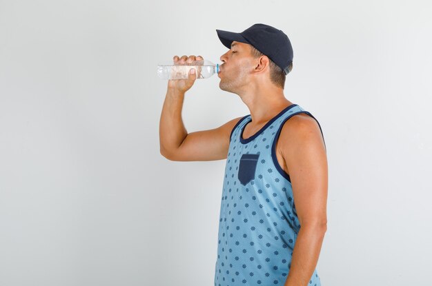 Joven parado y bebiendo agua en camiseta azul