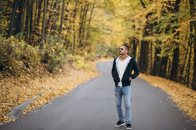 Joven parado en una carretera en un parque de otoño