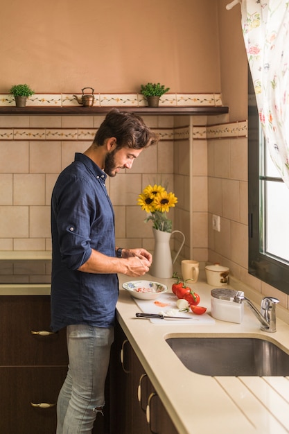 Joven parado en la cocina preparando ensalada