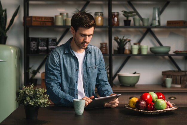 Joven parado detrás de la mesa mirando tableta digital