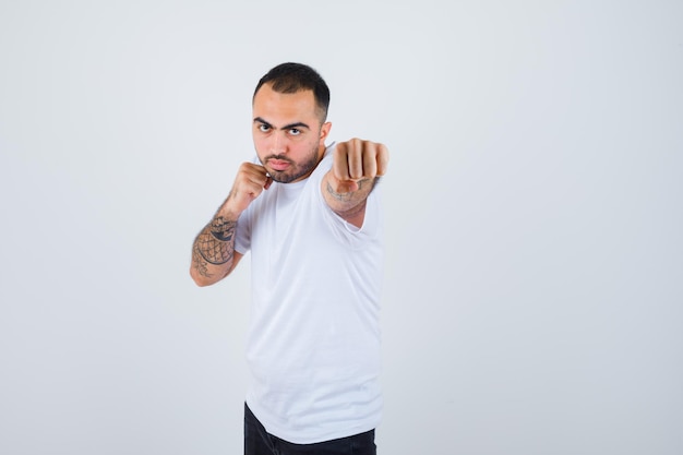 Joven parado en pose de boxeador en camiseta blanca y mirando poderoso