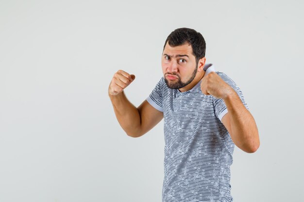 Joven parado en pose de lucha en camiseta y mirando fuerte, vista frontal.