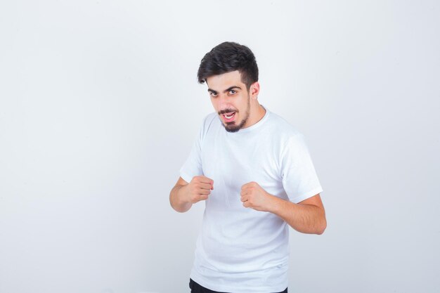 Joven parado en pose de lucha pose en camiseta y mirando rencoroso