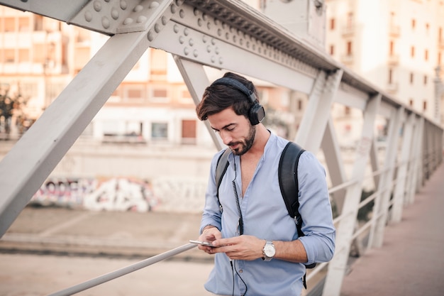 Foto gratuita joven parado en el puente escuchando música con smartphone