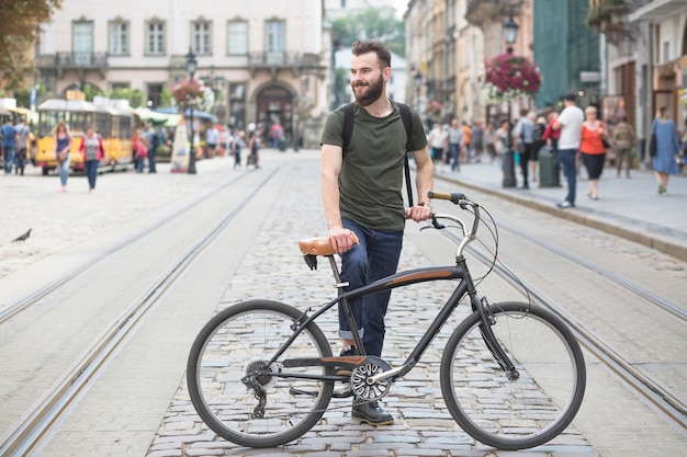 Foto gratuita joven parado con su bicicleta en la ciudad