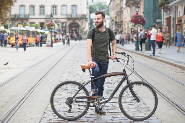 Joven parado con su bicicleta en la ciudad