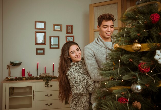 Joven pareja abrazándose mientras decoraba un árbol de navidad