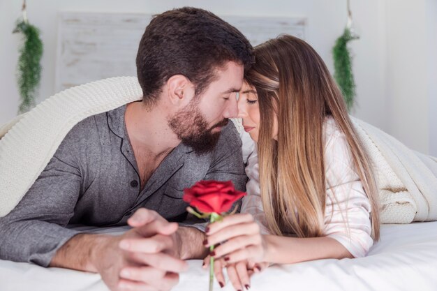 Joven pareja acostada en la cama con rosa