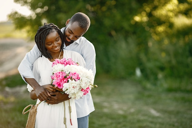 Joven pareja africana en abrazo romántico en un campo. Amantes jóvenes en un campo con flores.