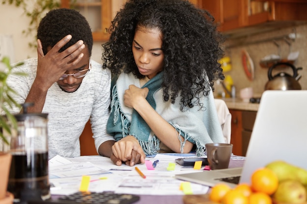 Joven pareja afroamericana con muchas deudas calculando facturas de gas y electricidad