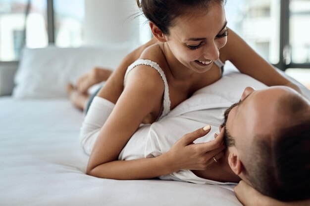 Joven pareja amorosa disfrutando de su mañana mientras se acuesta en la cama y habla