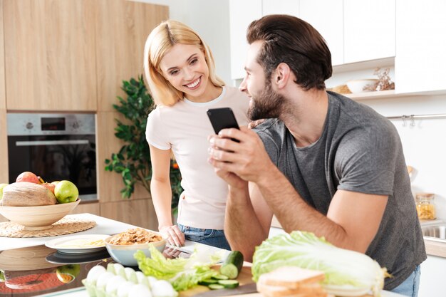 Joven pareja amorosa feliz cocinando juntos usando el teléfono