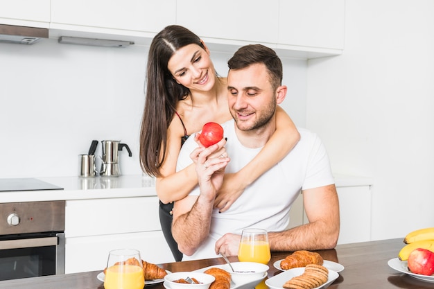 Joven pareja amorosa sosteniendo la manzana en la mano mientras desayunando