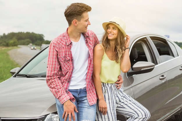 Foto gratuita joven pareja apoyándose en la capucha del coche mirando el uno al otro