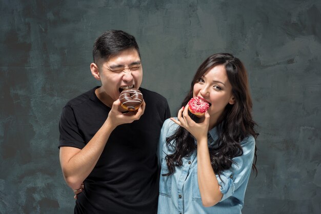 Joven pareja asiática disfruta comiendo de donut colorido dulce