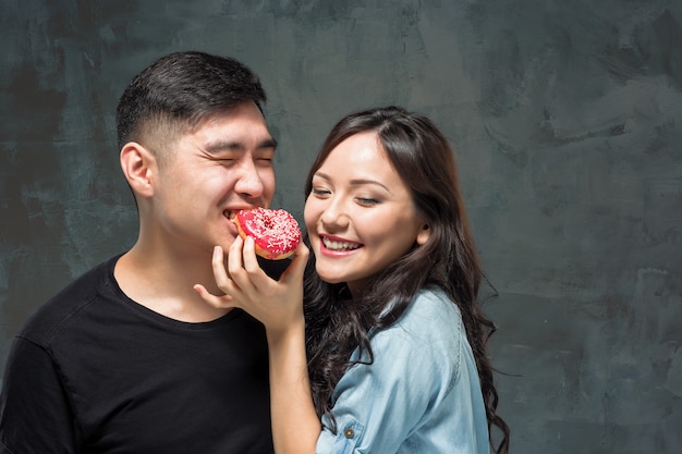 Joven pareja asiática disfruta comiendo de donut colorido dulce
