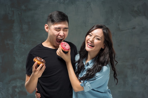 Joven pareja asiática disfruta comiendo de donut colorido dulce