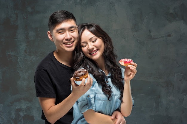 Joven pareja asiática disfruta comiendo dulce donut colorido