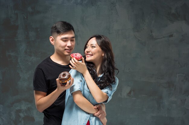 Joven pareja asiática disfruta comiendo dulce donut colorido