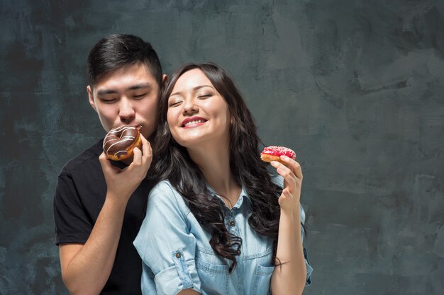 Joven pareja asiática disfruta comiendo dulce donut colorido
