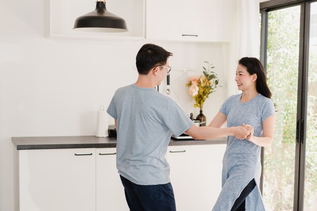 Joven pareja asiática escucha música y baile después de desayunar en casa. Atractiva mujer japonesa y hombre guapo están disfrutando pasar tiempo juntos en la cocina moderna en casa por la mañana.