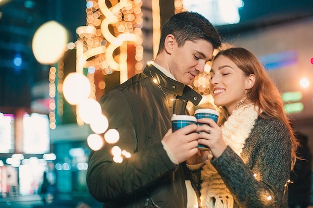 Joven pareja besándose y abrazándose al aire libre en la calle de noche en Navidad