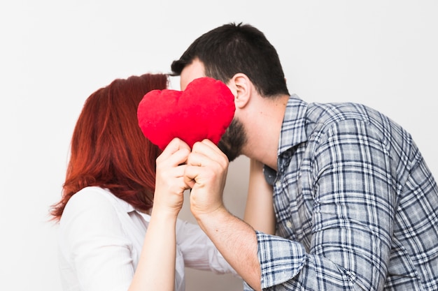 Joven pareja besándose detrás de corazón rojo