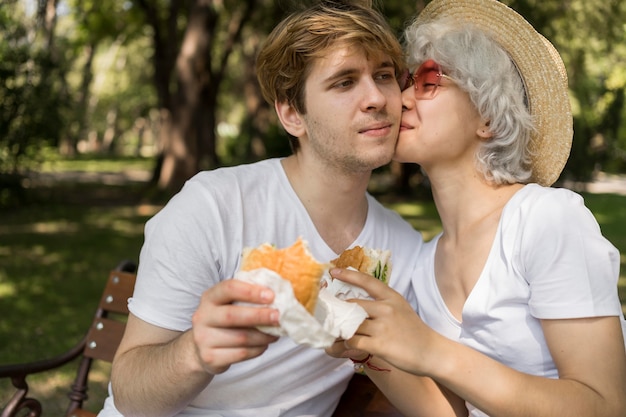 Joven pareja besándose mientras come hamburguesas en el parque